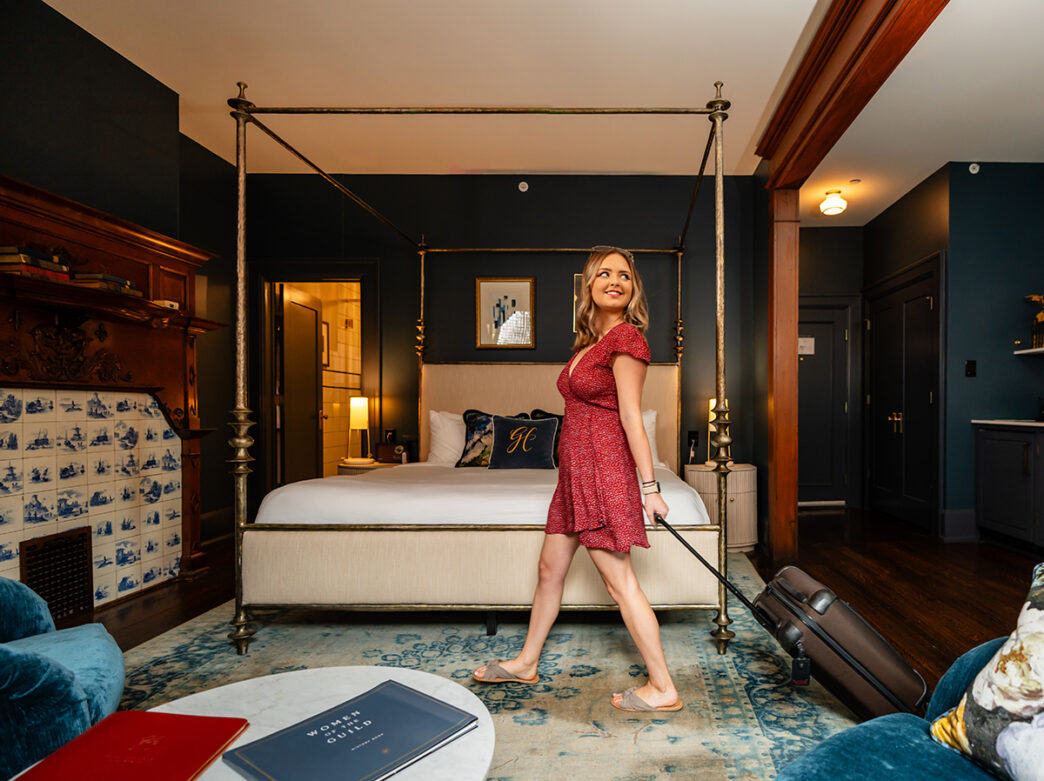 A woman in a red dress rolls her suitcase through a guest room at Guild House Hotel in Philadelphia.