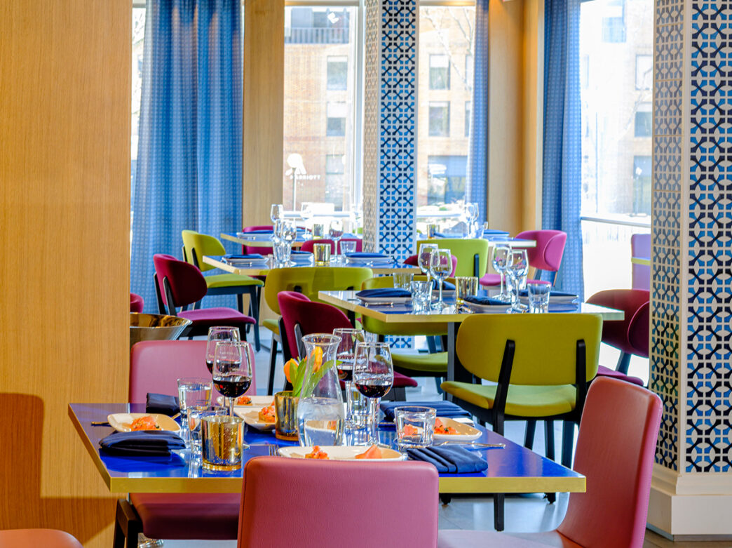 Colorful dining room with pink and green dining chairs and blue curtains filled with natural light at Positano Coast in Philadelphia.