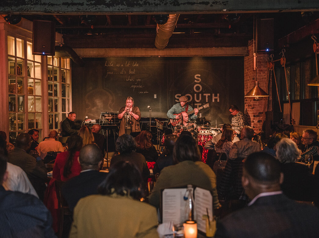 A crowd watches from cafe tables as a jazz band performs on stage at SOUTH in Philadelphia.