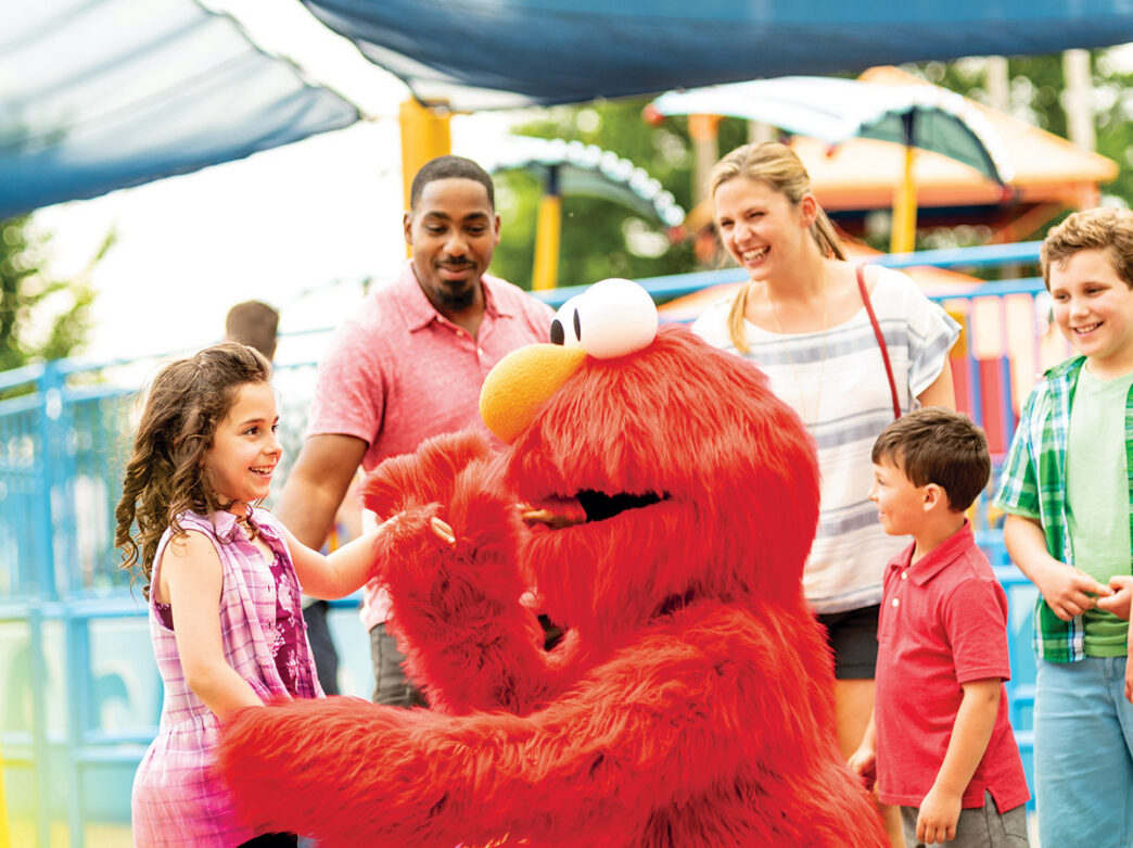 Elmo saluda a una familia vestida informalmente que pasea por Sesame Place.