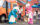 A casually dressed mother watches as her two daughters hug Cookie Monster and his fuzzy pink friend.