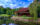 An image of a house, pond and garden at the Shofuso Japanese Cultural Center surrounded by green trees and grass.