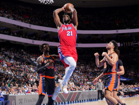 Joel Embiid of the 76ers jumps with a basketball towards the hoop while three players on the Knicks watch.