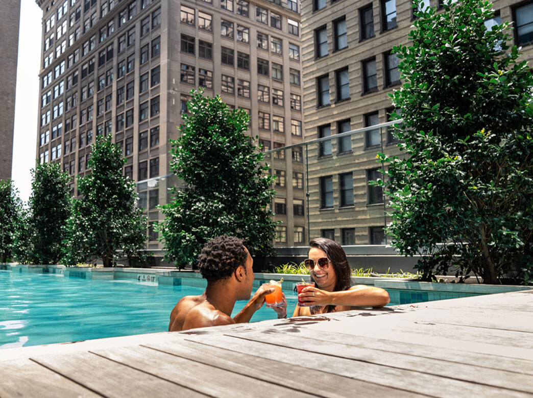 Two people lounge in the rooftop pool at The W in Philadelphia while drinking cocktails.