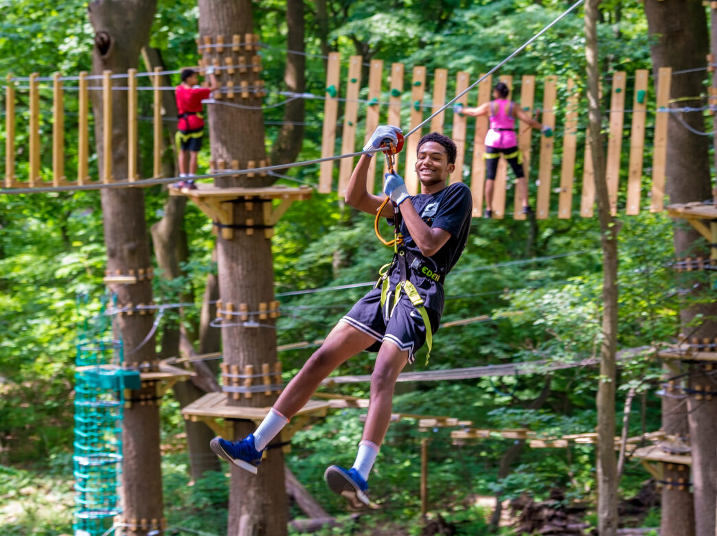 A teenager wearing a harness is suspended along a zipline at TreeTop Quest in Philadelphia.