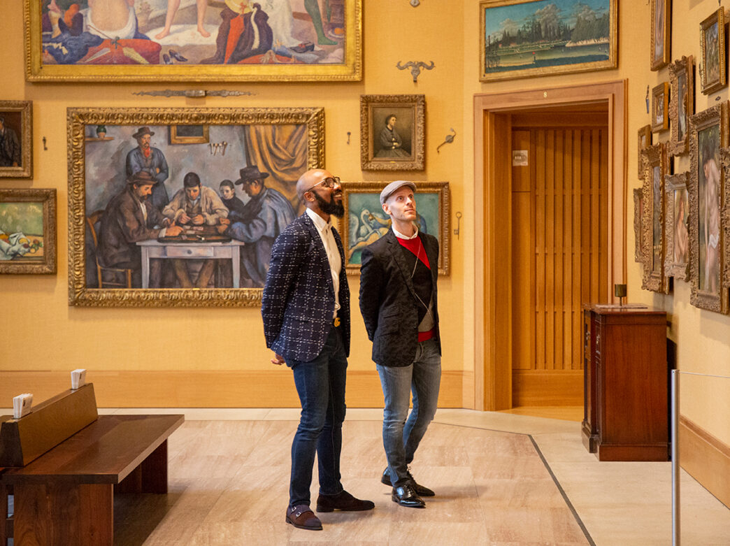 Two people wearing blazers and jeans look up at framed artwork in a gallery at the Barnes Foundation.