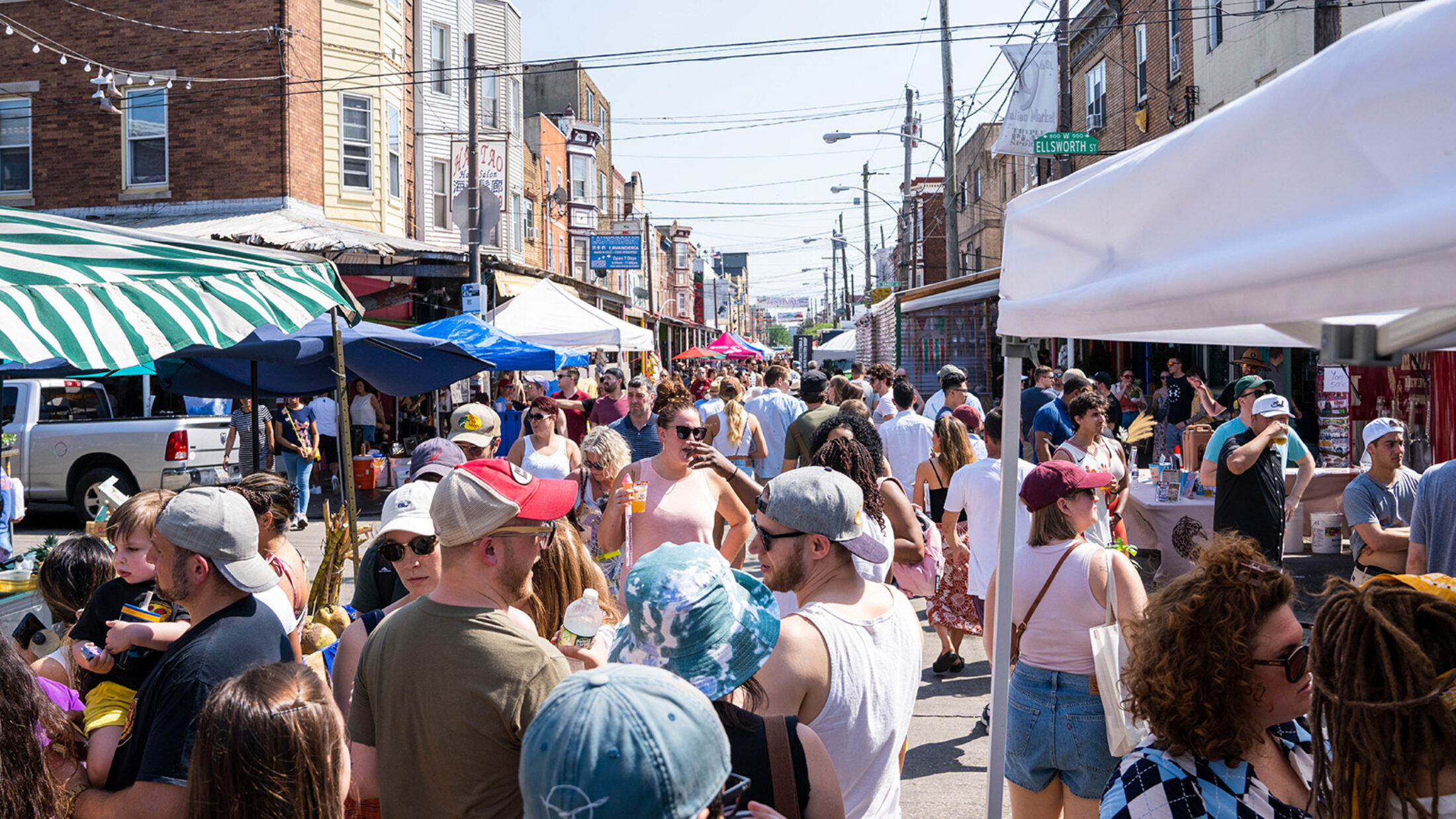 A crowd of casually dressed festival-goers enjoy food and drink from vendors on Ninth Street during the 9th Street Italian Market Festival.