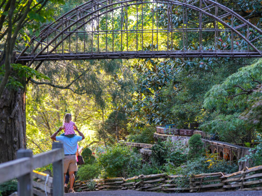 A father carries a child on their shoulders as they walk past the Garden Railway model trail at Morris Arboretum in Philadelphia.