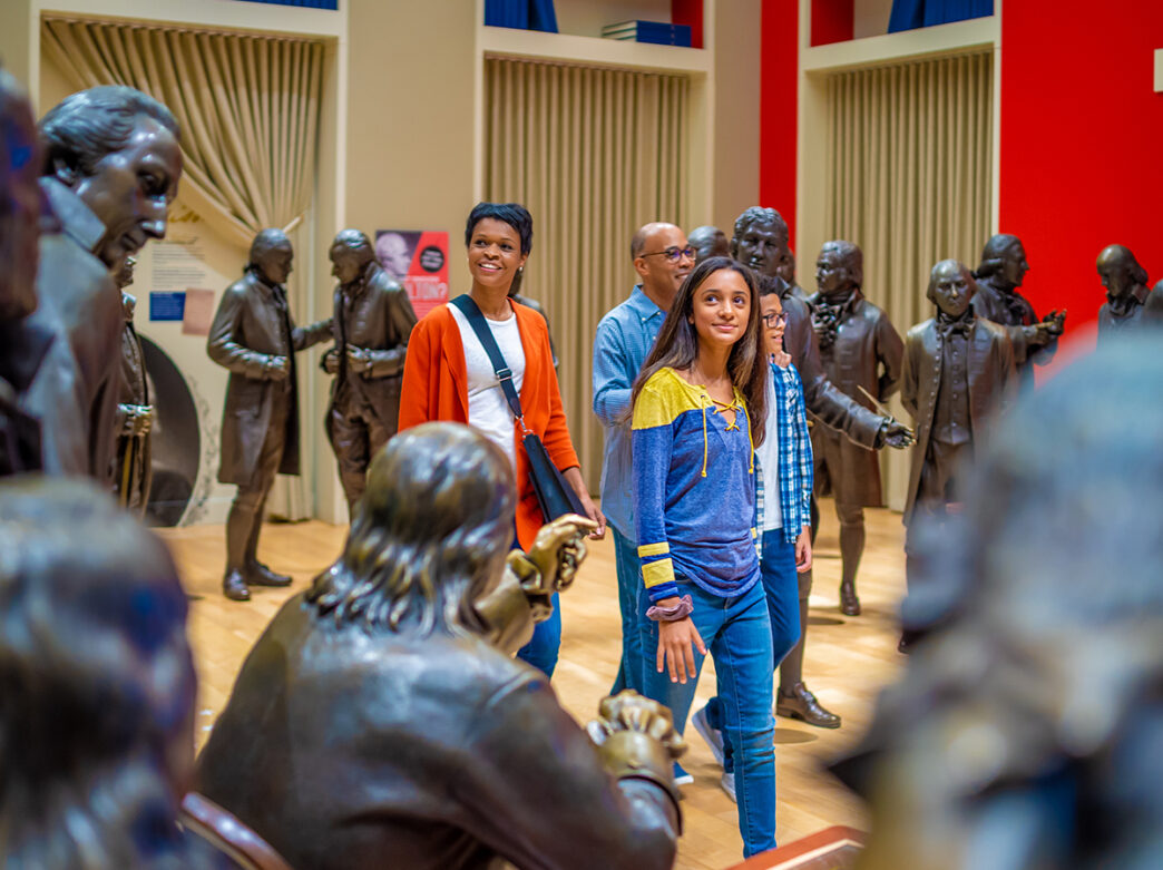 A family walks through a room of life-sized bronze statues of the Founding Fathers at the National Constitution Center.