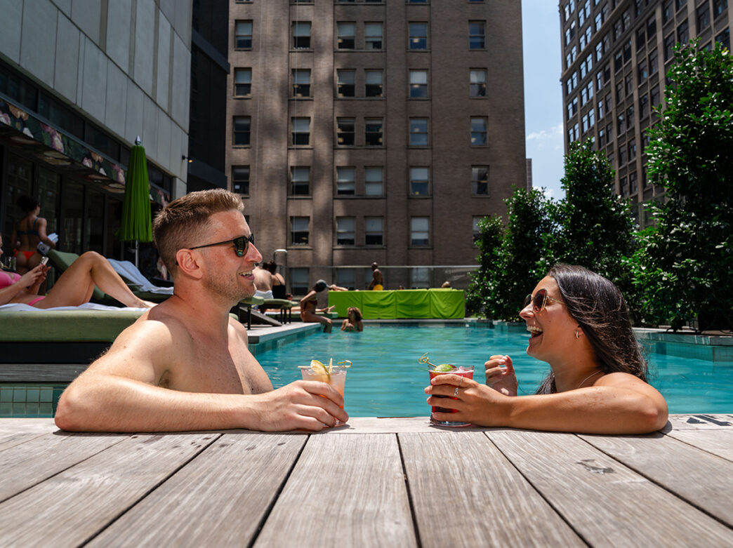 Two people relax in the pool at The W in Philadelphia. They both wear sunglasses and hold a drink in their hands.