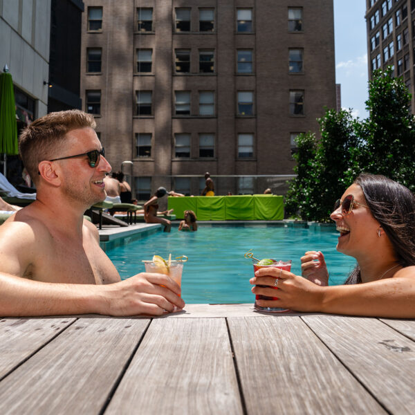 Two people relax in the pool at The W in Philadelphia. They both wear sunglasses and hold a drink in their hands.