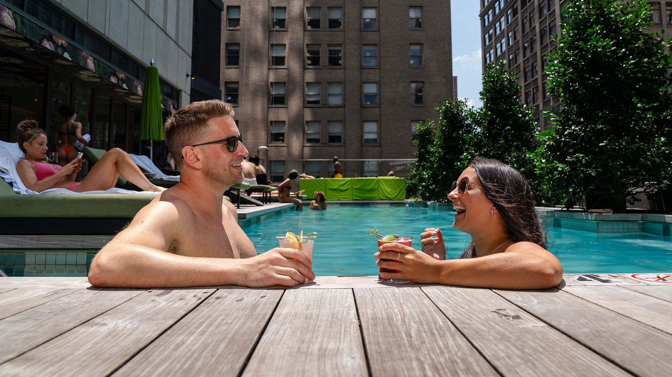 Two people relax in the pool at The W in Philadelphia. They both wear sunglasses and hold a drink in their hands.