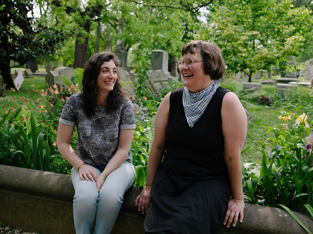 Two people sit on a concrete wall in front of the Grave Gardens at The Woodlands Cemetery and Mansion.