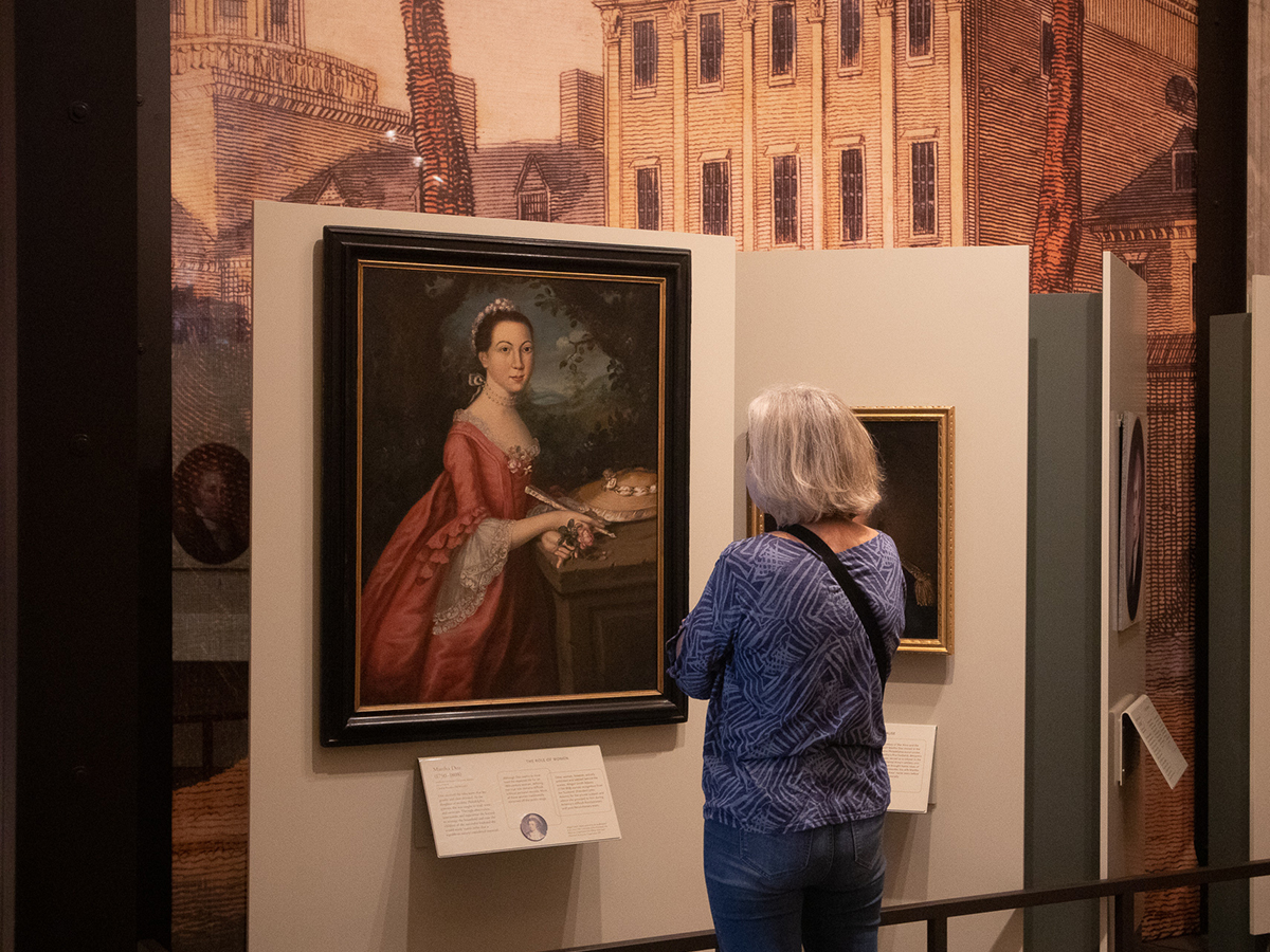 A visitor stands with their back to the camera while examining a portrait of a Martha Doz hanging in a gallery exhibit.