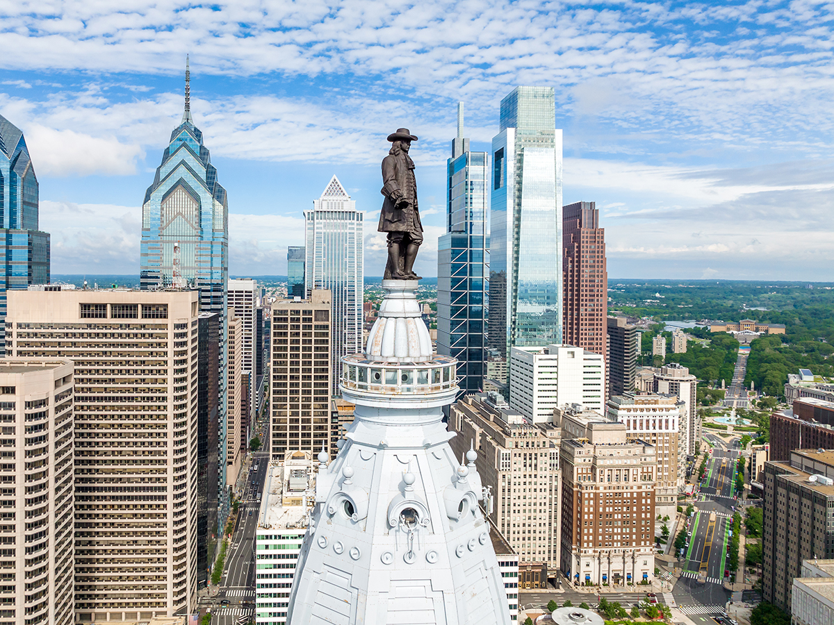 A drone view of the William Penn statue atop City Hall with the Philadelphia city skyline in the background.