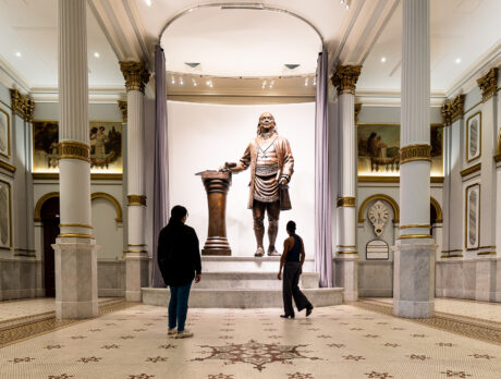 Two people look up at a large bronze statue of Benjamin Franklin displayed in the Masonic Temple in Philadelphia.