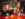 Two people sit at a table with a red tabletop and cheers their drinks while laughing at Tattooed Mom in Philadelphia.