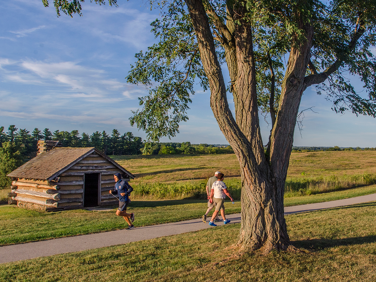 People walk and run along a paved trail through a meadow at Valley Forge National Park.