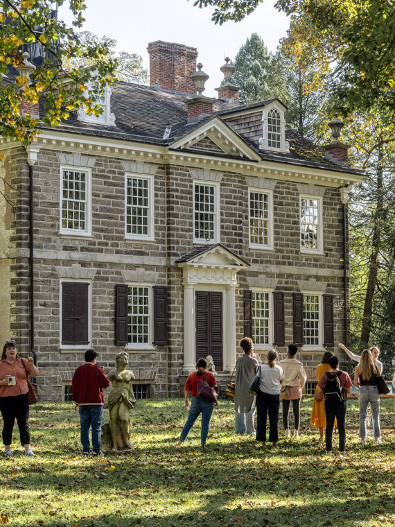Group of people stand outside on the lawn in front of the Carriage House at Cliveden.