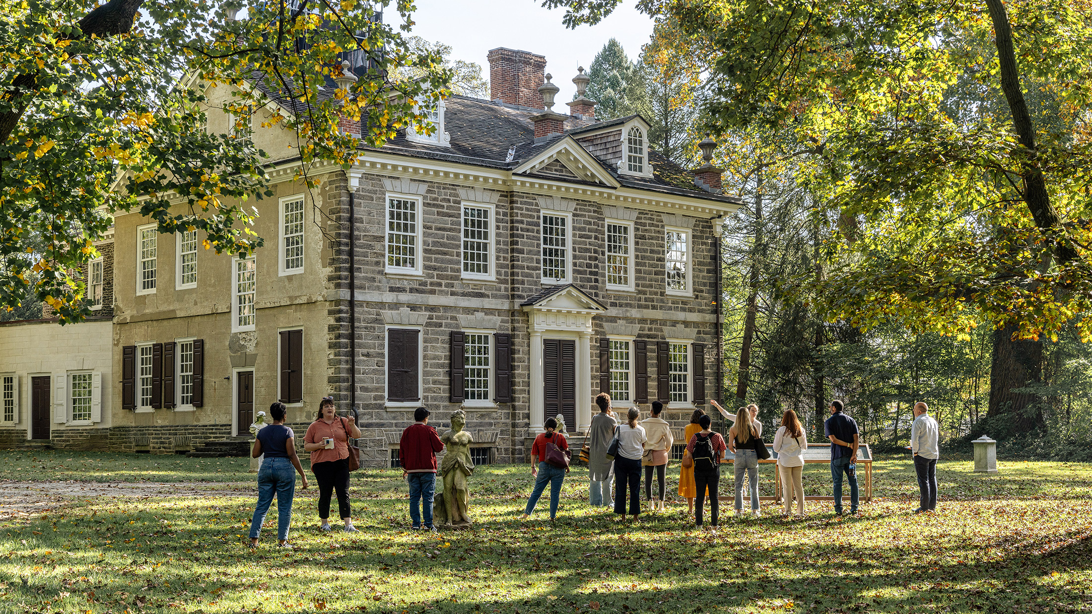Group of people stand outside on the lawn in front of the Carriage House at Cliveden.