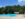 People swim in a large outdoor swimming pool with lifeguard stands and a pavilion near the pool.