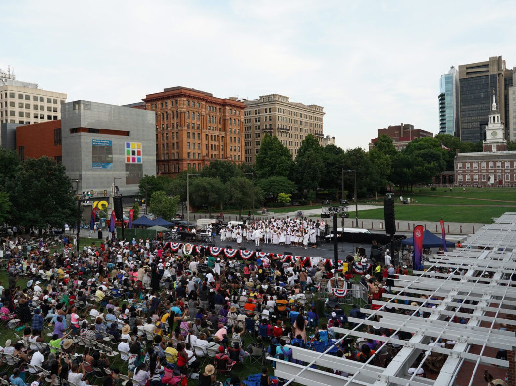Un groupe gospel tout de blanc vêtu se produit sur scène devant une foule nombreuse à Independence Mall dans le cadre du Wawa Welcome America.
