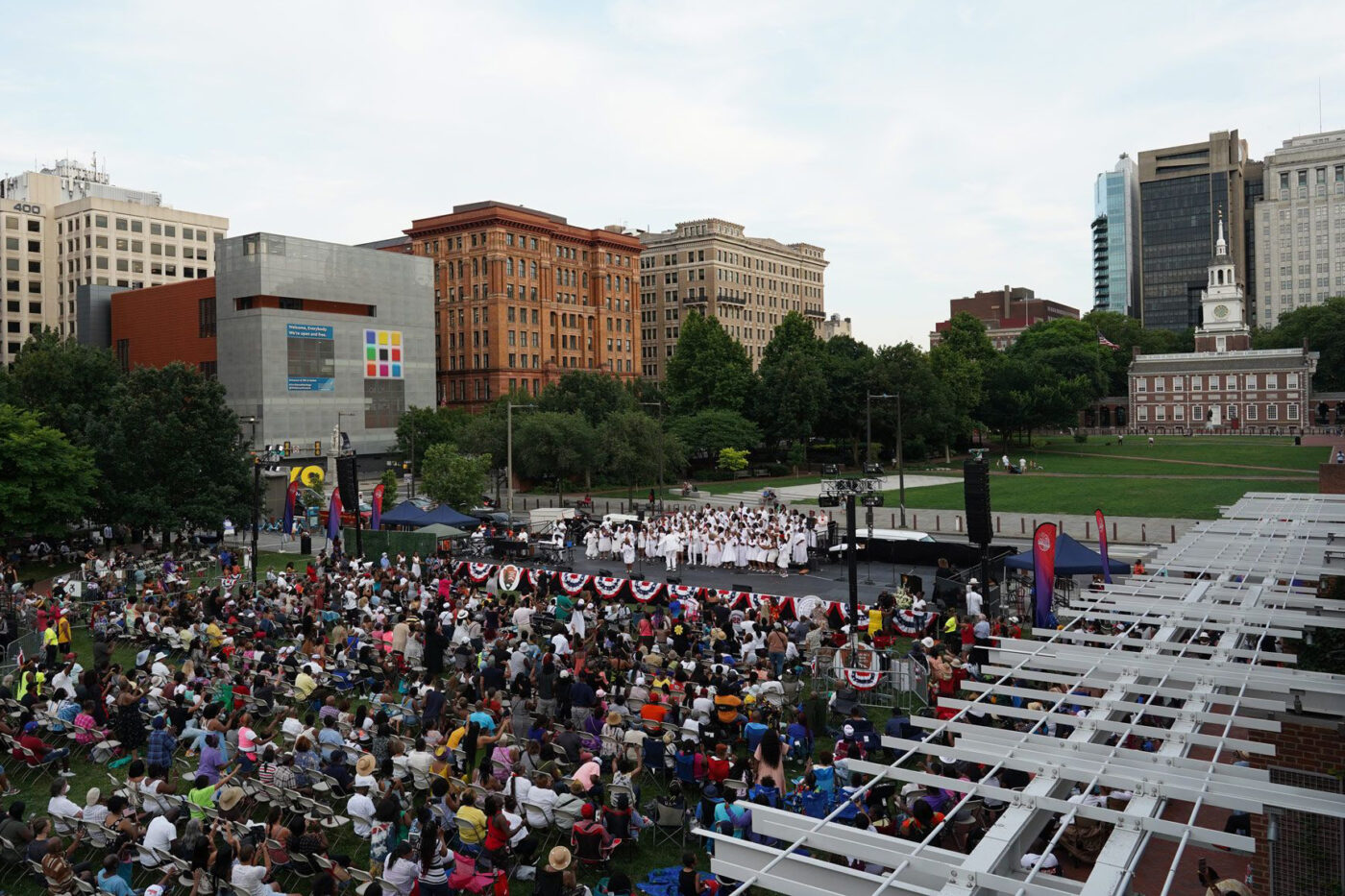 A gospel group wearing all white performs on stage in front of a large crowd on Independence Mall for Wawa Welcome America.