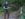 A hiker wearing a blue hat, black shirt and brown hiking pants holds hiking poles while posing for a photo near a trail marker in Wissahickon Valley Park.