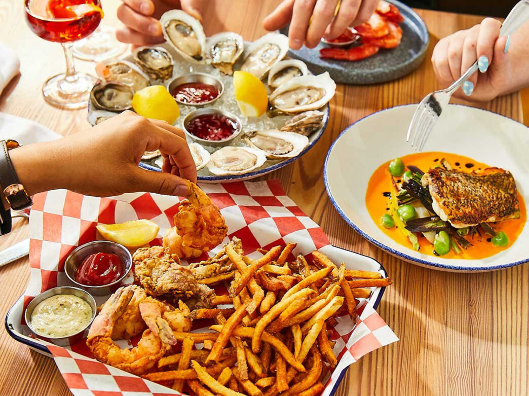 People reach for food items on the table at Oyster House, including oysters, shrimp, fries and fish.