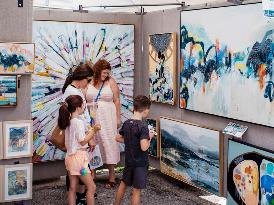 Two women and two children admire abstract paintings displayed in a vendor tent at the Manayunk Arts Festival.