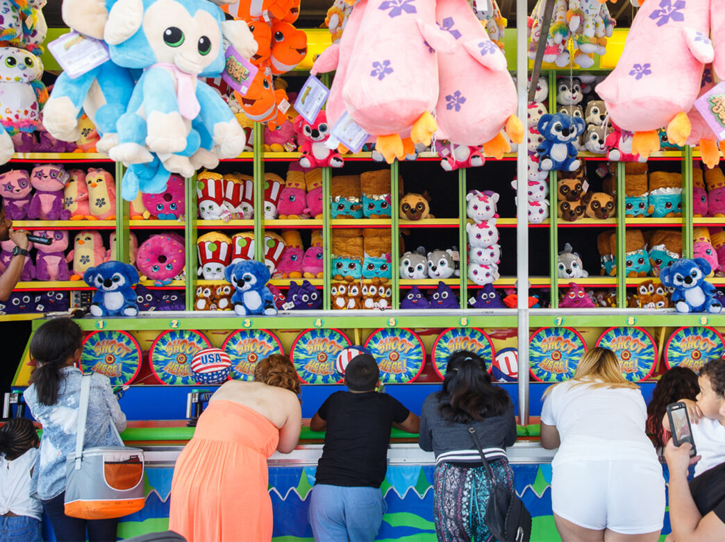 People line up at a water gun water shooting arcade game while a staff referee speaks into a microphone at the RiverRink Summerfest in Philadelphia.