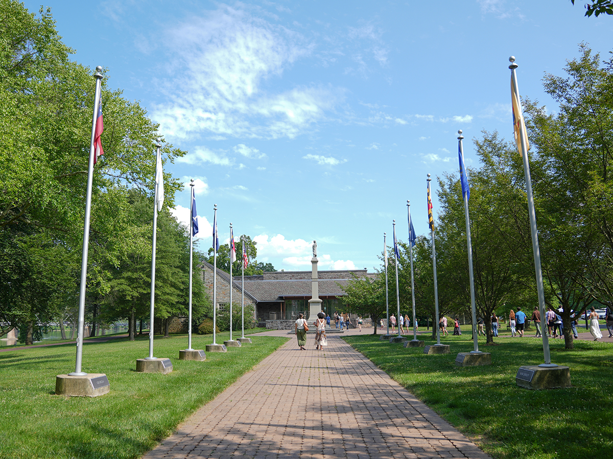 Two people walk down a brick walkway lined with flagpoles towards a building at Washington Crossing Historic Park.