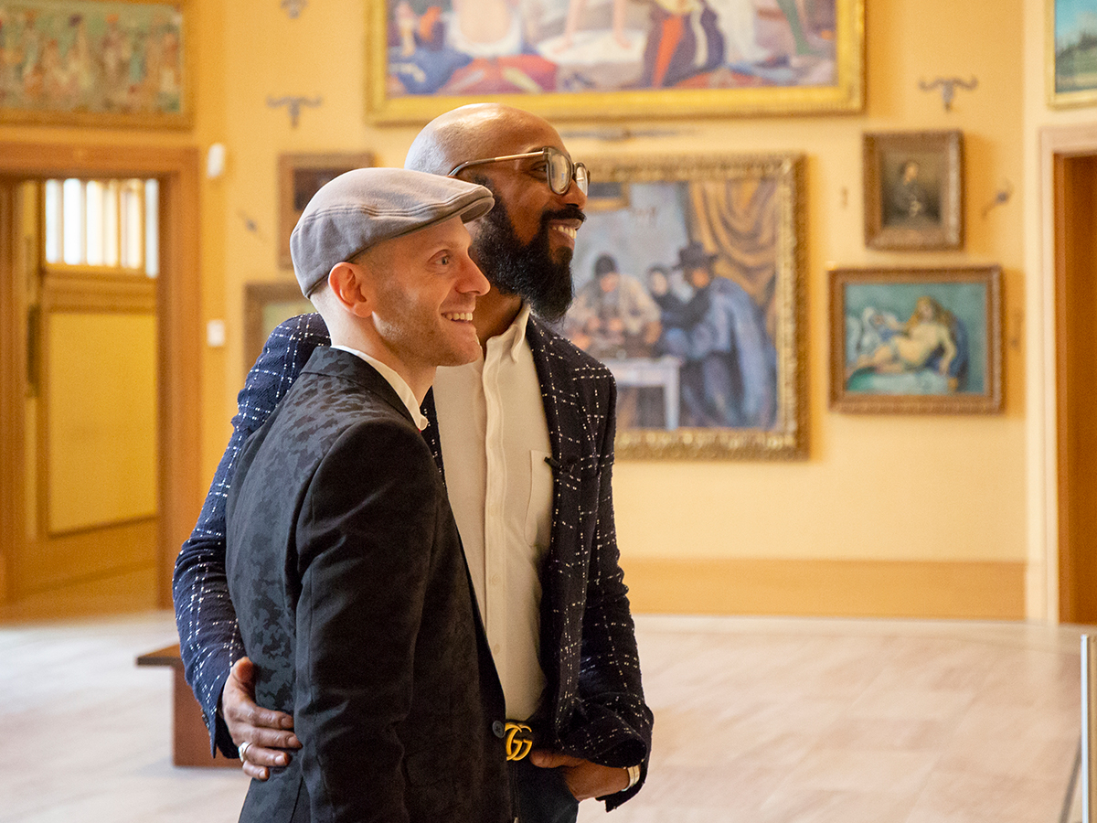 Two people wearing blazers smile and look at framed artwork in a gallery at the Barnes Foundation.