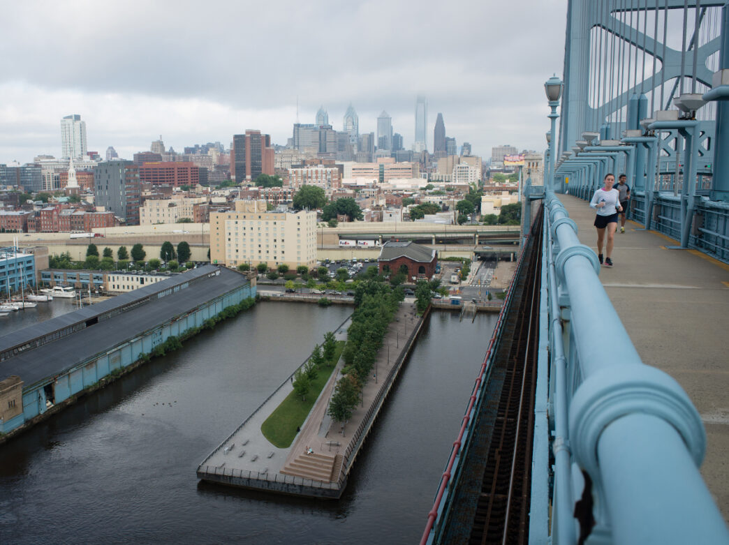People walk and run on the Benjamin Franklin Bridge over Delaware River with the Philadelphia skyline in the background.