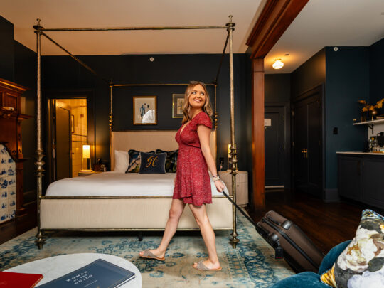 A woman in a red dress rolls her suitcase through a guest room at Guild House Hotel in Philadelphia.