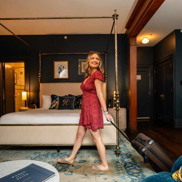 A woman in a red dress rolls her suitcase through a guest room at Guild House Hotel in Philadelphia.