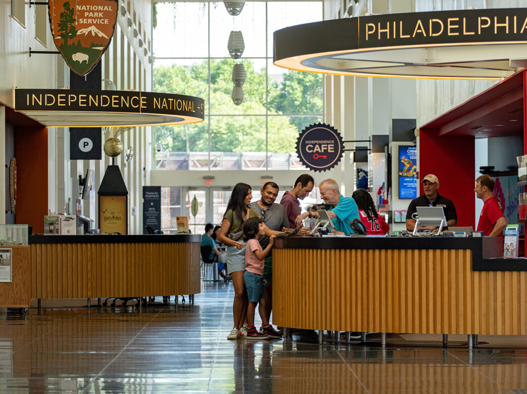 People stand at an information desk and speak to a staff member in Philadelphia Independence Visitor Center.