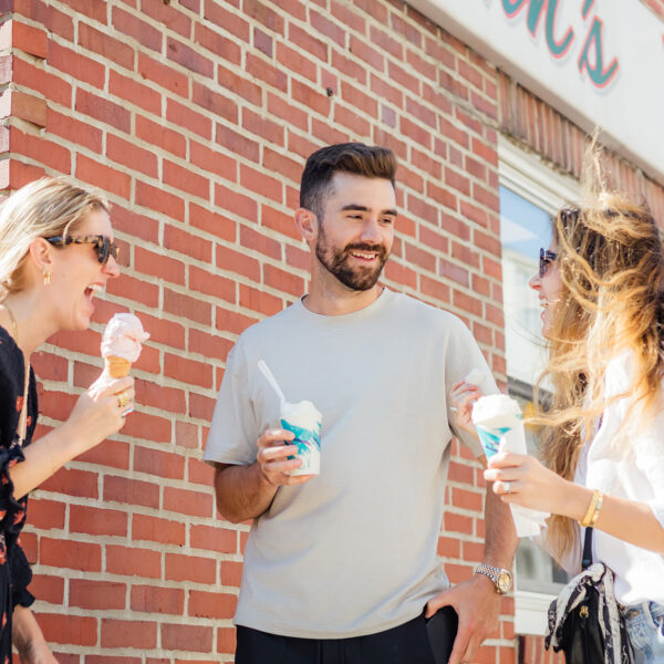 Three people stand in a group outside John's Water Ice laughing and eating water ice and ice cream.