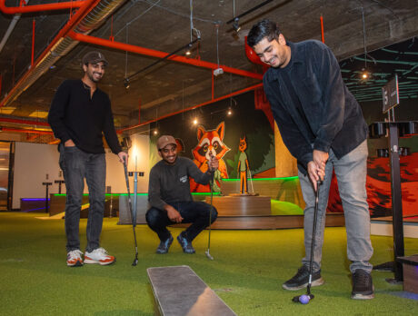 Un groupe de jeunes hommes vêtus de tenues décontractées noires et grises sourient en jouant une partie de minigolf au Libertee Grounds.