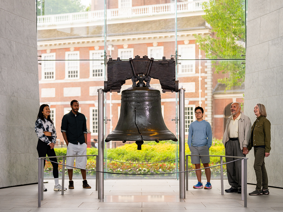 Five people stand around and observe the Liberty Bell at Liberty Bell Center.