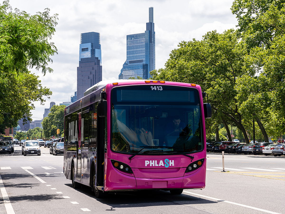 A pink and purple PHLASH bus drives down the street with the Comcast Center and Comcast Technology Center in the background.