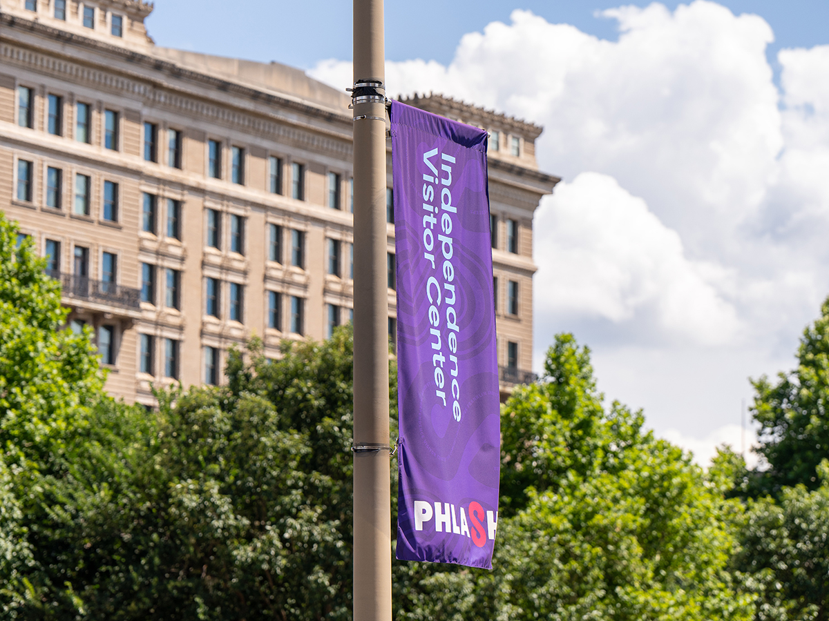 A purple sign hangs from a telephone pole with the PHLASH logo and Independence Visitor Center written on the flag.
