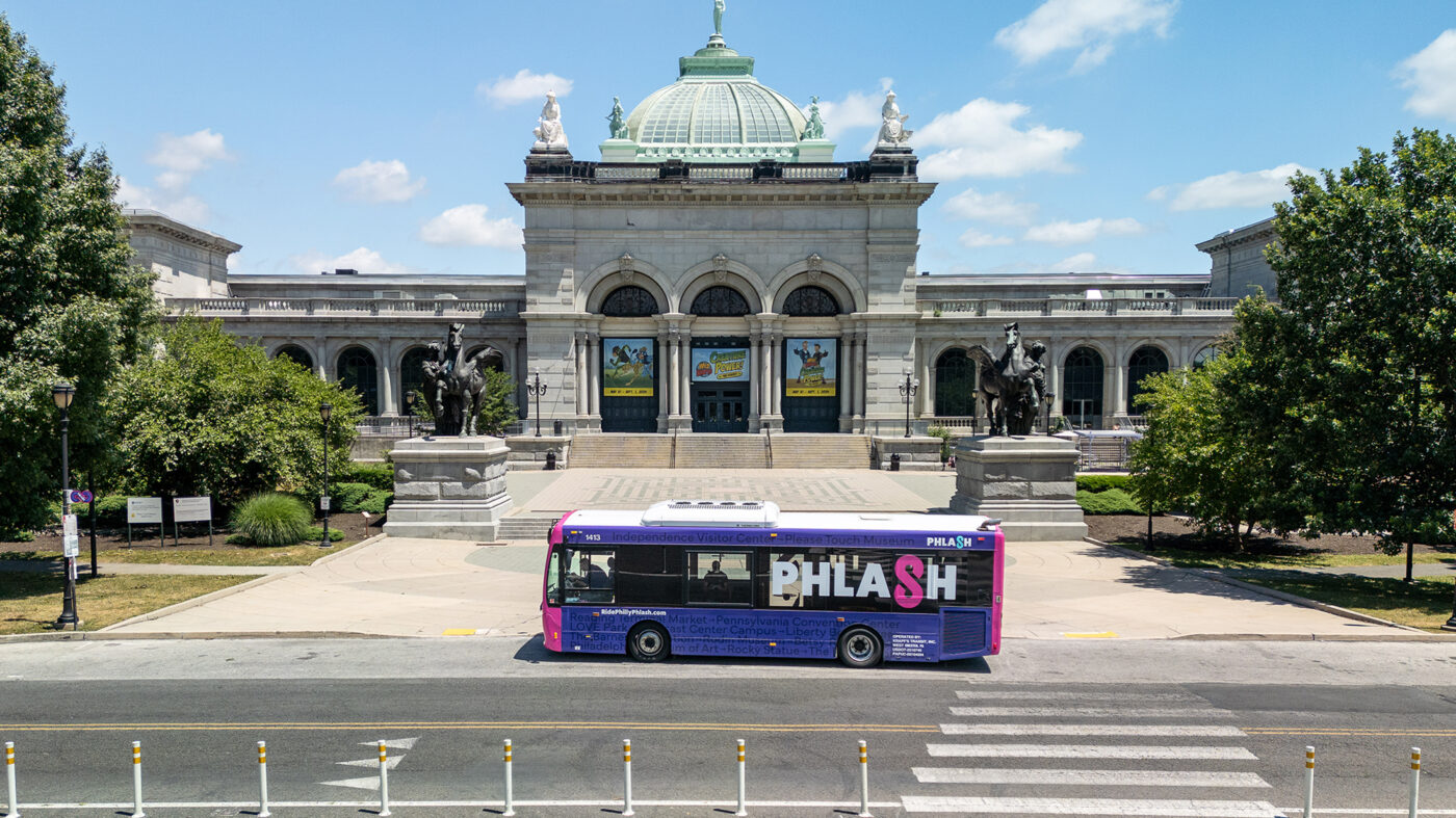 A pink and purple PHLASH bus stops in front of the Please Touch Museum in Philadelphia.