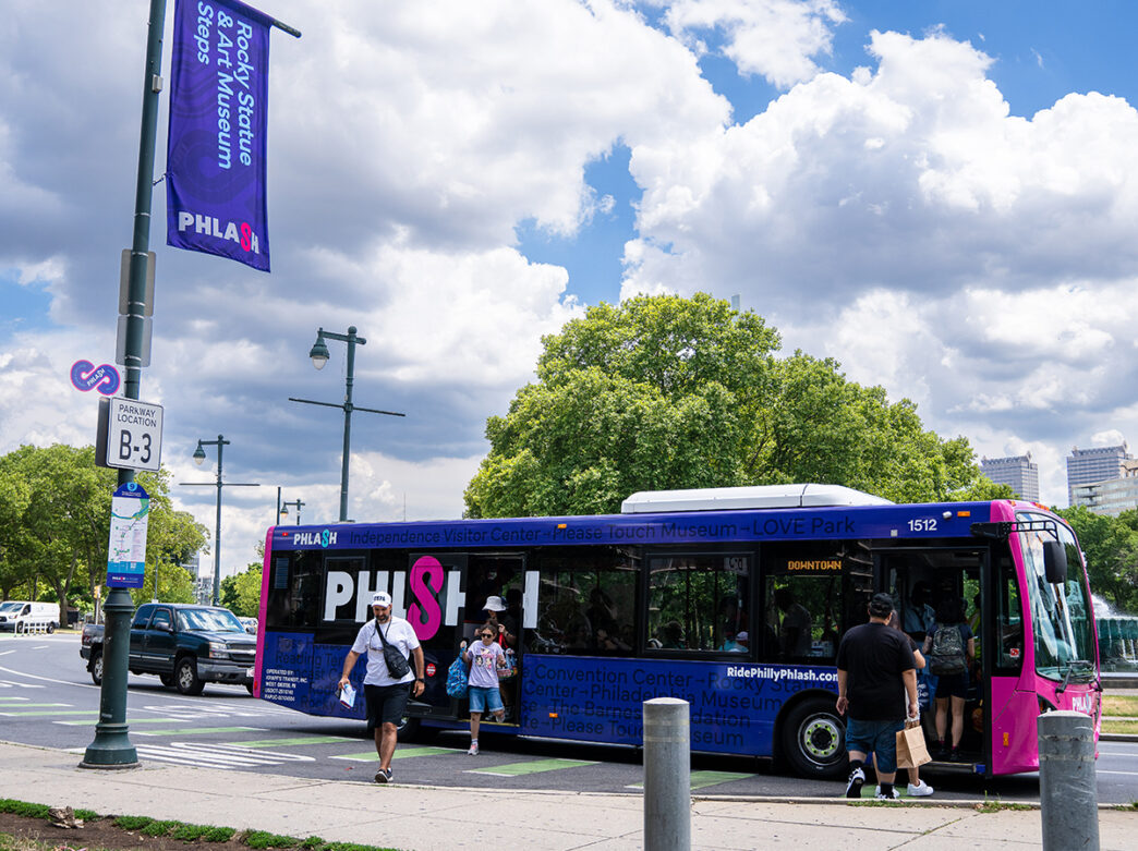 La gente sube y baja de un autobús PHLASH rosa y morado cerca del Rocky State y las escaleras del Museo de Arte de Filadelfia.