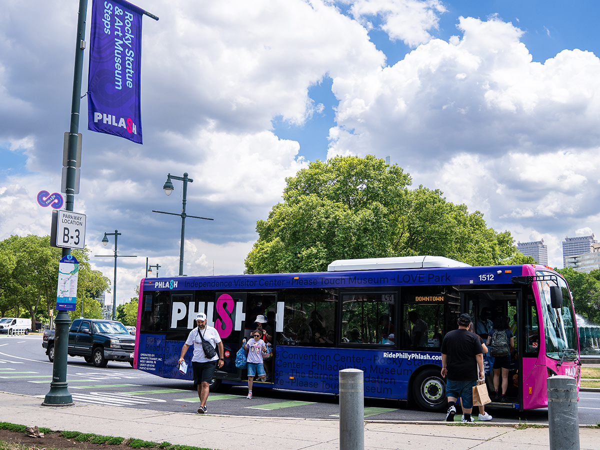 People depart and board a pink and purple PHLASH bus near the Rocky State and Art Museum Steps in Philadelphia.