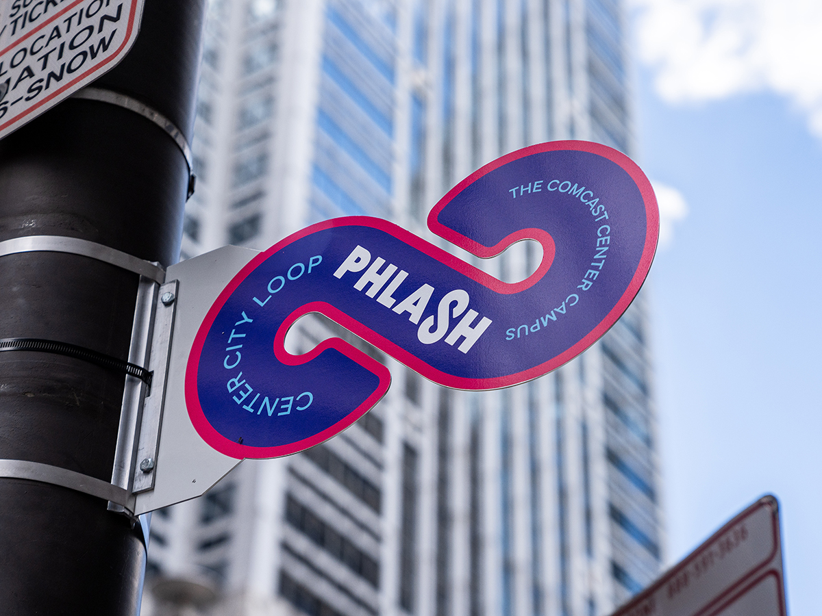A purple, pink and teal PHLASH sign on a telephone pole.