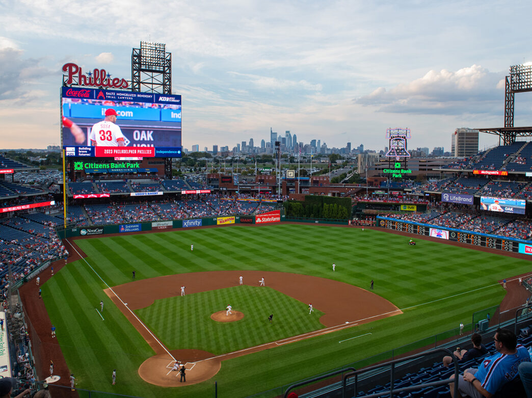A view of a baseball field, people in the stadium and the Philadelphia city skyline in the distance.