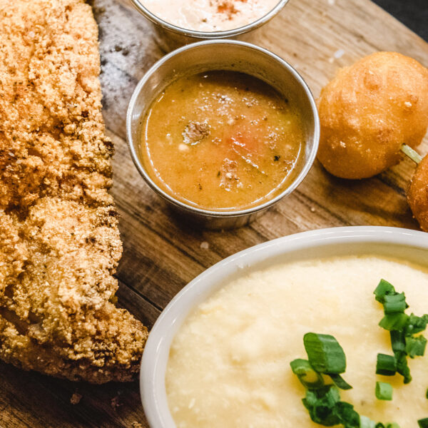 Een heerlijk ogend assortiment van meerval, aardappelpuree, hush puppies en dipsauzen staat op een houten bord bij SOUTH.
