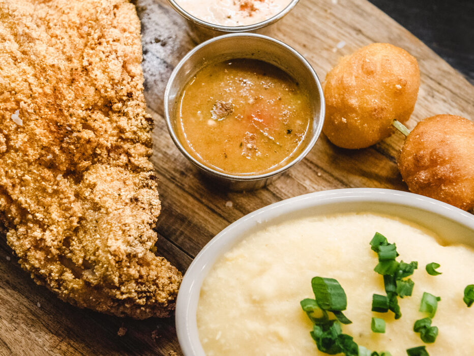 Un delicioso surtido de bagre, puré de patatas, hush puppies y salsas para mojar en un plato de madera en SOUTH.