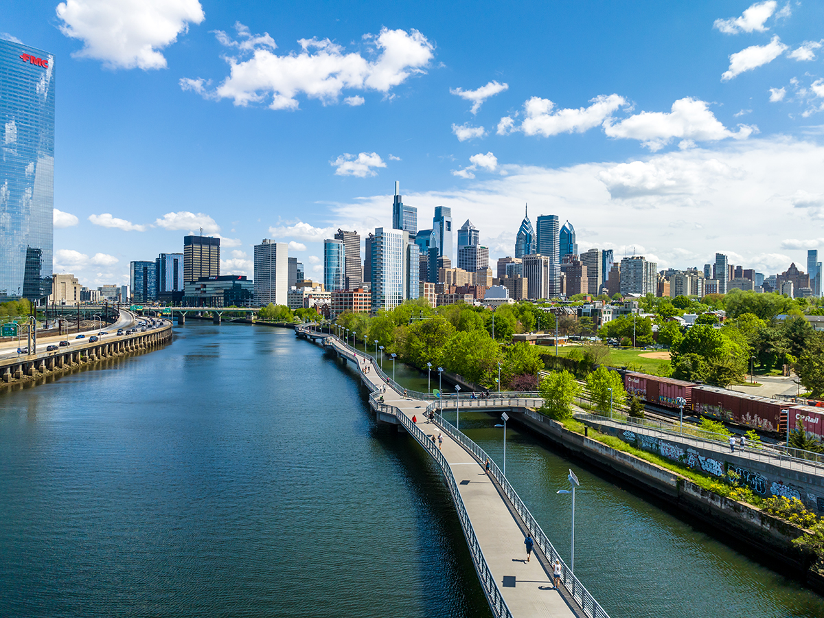 The Philadelphia skyline on a sunny day with the Schuylkill River and Schuylkill Banks Boardwalk in the foreground.
